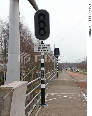 Lights at a bridge, sign saying 'Bij belsignaal brugdek vrijmaken - Clear the road when bell rigns' Lights at a bridge, sign saying 'Bij belsignaal brugdek vrijmaken - Clear the road when bell rigns' 111987494