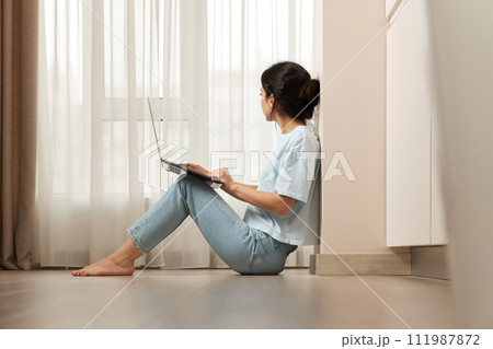 casual woman sitting on the floor and working on laptop at home 111987872