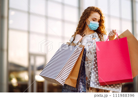 Woman in shopping. Young girl in protective sterile medical mask on her face with shopping bags. Woman in shopping. Young girl in protective sterile medical mask on her face with shopping bags. 111988396