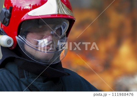 The face of a fireman in a helmet on a background of fire. Putting out a fire. The face of a fireman in a helmet on a background of fire. Putting out a fire. 111988476