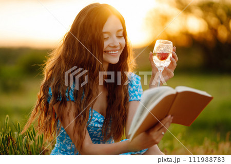 Young woman sits on a plaid with a book. Summer picnic in nature. Healthy food. 111988783