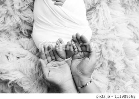 The palms of the father, the mother are holding the foot of the newborn baby. Feet of the newborn on the palms of the parents. Studio macro black and white photo of a child's toes, heels and feet. 111989568