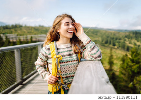 Young woman traveler walking across bridge in middle of forest. Travel and active lifestyle concept. 111990111