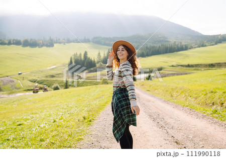 Happy female traveler exploring area in green valley with mountains in background. Concept of nature 111990118