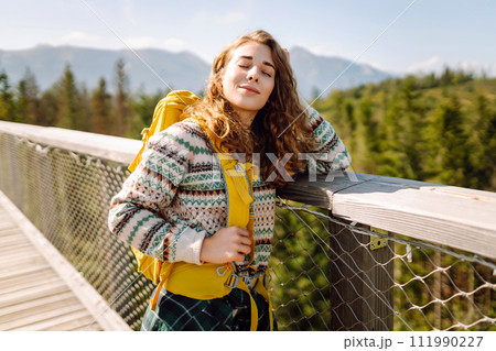 Young woman traveler walking across bridge in middle of forest. Travel and active lifestyle concept. 111990227