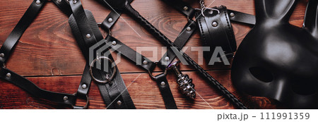 set of BDSM sex toys with handcuffs, whip flogger, butt anal plug for submission and domination on wooden background 111991359
