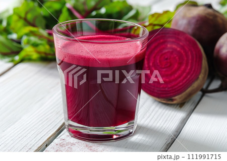 Fresh beetroot juice in a glass on white wood, with whole and sliced beets in the background Fresh beetroot juice in a glass on white wood, with whole and sliced beets in the background 111991715