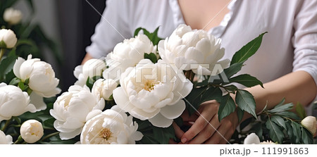 A female florist collects a bouquet of pions- fresh cut flowers in boxes and vases in a warehouse and racks for sale, delivery for the holiday. Spring, March 8, women's Day, birthday. AI generated 111991863