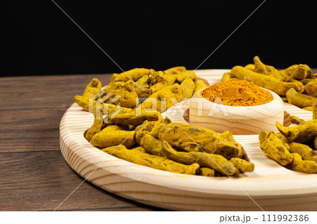 Turmeric powder and dried turmeric root on a black background Turmeric powder and dried turmeric root on a black background 111992386