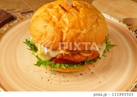 Cheeseburger topped with lettuce and various toppings placed on a plate, ready to be enjoyed. Cheeseburger topped with lettuce and various toppings placed on a plate, ready to be enjoyed. 111993503