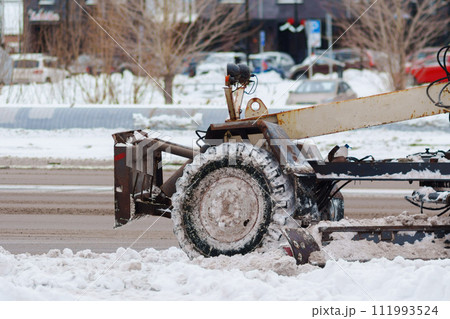 Snow plow is parked on the side of the road, its powerful presence contrasting with the stillness of the winter landscape. 111993524