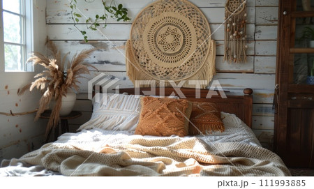 A wicker dreamcatcher hangs over a wooden bed with a white crocheted bedspread in boho style 111993885