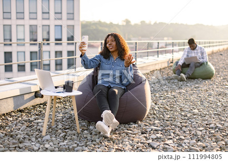 African woman in casual denim shirt using phone while recording video. 111994805