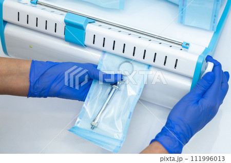 Dentist hands in blue gloves holding dentist tools doing sterilization of instruments Dentist hands in blue gloves holding dentist tools doing sterilization of instruments 111996013
