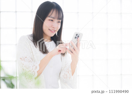 座ってスマホを持つ笑顔の若い女性の 緑の前ボケあり 座ってスマホを持つ笑顔の若い女性の 緑の前ボケあり 111998490
