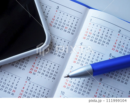 テーブルに置かれた手帳とカレンダーとスマートフォン 111999104