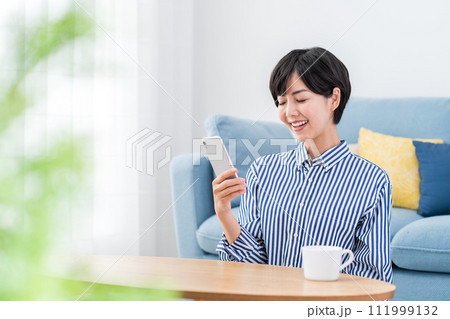 リビングでスマホを操作する女性。 リビングでスマホを操作する女性。 111999132