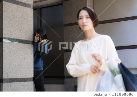 建物に隠れて女性の写真を撮る人 111999696
