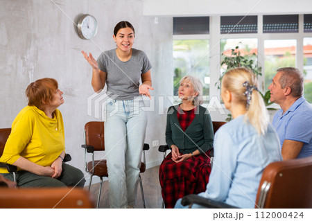 Young female teacher explaining subject to mature students 112000424