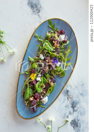 top view organic baby greens salad with beetroot, goat cheese, pistachios and citrus dressing 112000425