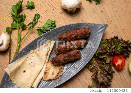 Top view of delicious kebabs lula lamb kebab with grilled vegetables and herbs on a wooden table. Top view of delicious kebabs lula lamb kebab with grilled vegetables and herbs on a wooden table. 112000428