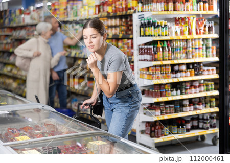 Young woman looking at products in glass refrigerator in store 112000461
