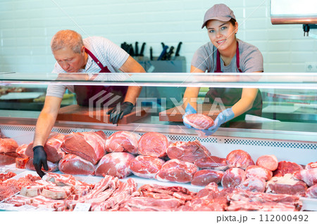 Positive young saleswoman vendor in apron and disposable gloves shows meat tenderloin Positive young saleswoman vendor in apron and disposable gloves shows meat tenderloin 112000492