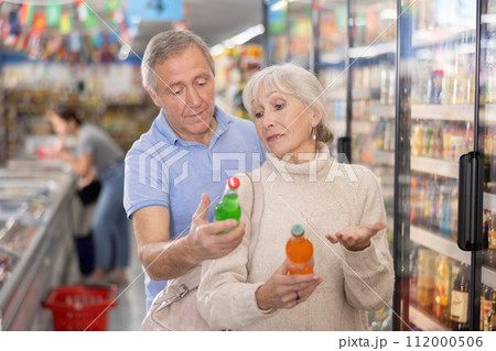 Elderly couple choosing sweet sodas together in the grocery section of supermarket 112000506