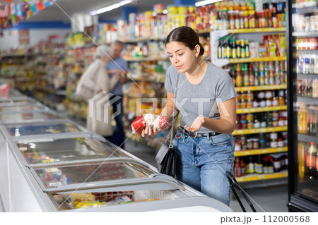 Woman choosing frozen food in supermarket. Woman purchasing goods in grocery store 112000568