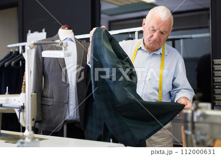 Professional tailor inspects mens jacket before starting work in workshop 112000631