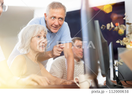 Friendly elderly computer course teacher helping woman learn computer Friendly elderly computer course teacher helping woman learn computer 112000638