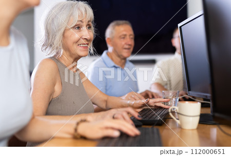 Smiling motivated older woman using computer at internet cafe Smiling motivated older woman using computer at internet cafe 112000651