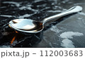 A classic silver spoon lies on a dark marbled surface with reflections. 112003683