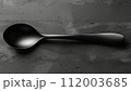 A matte black spoon on a textured grey concrete surface with subtle highlights. 112003685