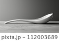 A modern, curved white spoon on a grey concrete background with soft lighting. 112003689