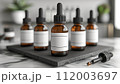 Multiple amber dropper bottles with blank white labels on a black slate coaster, in a modern kitchen setting. 112003697