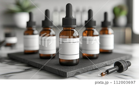 Multiple amber dropper bottles with blank white labels on a black slate coaster, in a modern kitchen setting. Multiple amber dropper bottles with blank white labels on a black slate coaster, in a modern kitchen setting. 112003697