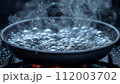 A close-up of a skillet on the stove with water boiling vigorously, showcasing the bubbles and steam in a kitchen setting. 112003702