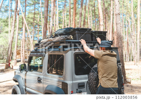 キャンプ場で車のルーフラックからキャンプ道具を降ろす男性キャンパー キャンプ場で車のルーフラックからキャンプ道具を降ろす男性キャンパー 112003856
