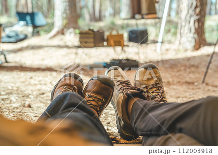 キャンプ場でテントの中に座るトレッキングブーツ・デニムスカートの女性と男性の足元 112003918