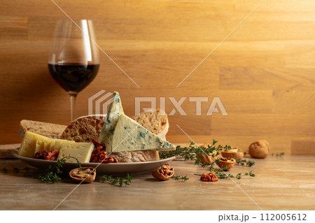 Cheese, bread, red wine, and walnuts on a kitchen table. 112005612