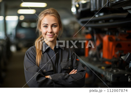 Confident female auto technician at garage, young woman mechanic stands in auto repair shop with crossed arms, represents professionalism and skills, gender diversity in automotive industry 112007874