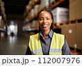 Professional female logistic manager in warehouse. Black woman in high-visibility jacket, overseeing warehouse operations. Strategic planning required to efficiency and meet demands in real-time 112007976