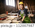 Smiling woman woodworker carpenter in protective gear works at workshop. Craftsmanship and Job Satisfaction, creating with one's hands, love of craft and positive work environment. 112007987