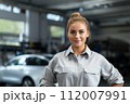 Smiling female technician in dealership. Professional young woman in car dealership smiles with confidence, embodying the shift towards a more inclusive and diverse automotive industry. 112007991