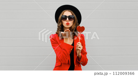 Beautiful stylish woman blowing kiss with sweet red heart shaped lollipop 112009366