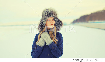 Portrait of beautiful blonde young woman posing in winter hat outdoors Portrait of beautiful blonde young woman posing in winter hat outdoors 112009416
