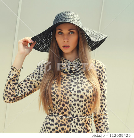 Portrait of beautiful blonde young woman wearing summer straw hat, leopard dress Portrait of beautiful blonde young woman wearing summer straw hat, leopard dress 112009429