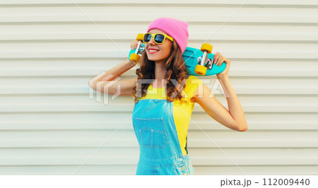 Summer portrait of happy smiling young woman with skateboard in colorful clothes Summer portrait of happy smiling young woman with skateboard in colorful clothes 112009440