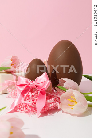 Chocolate egg with gifts and flowers on a light background 112010442